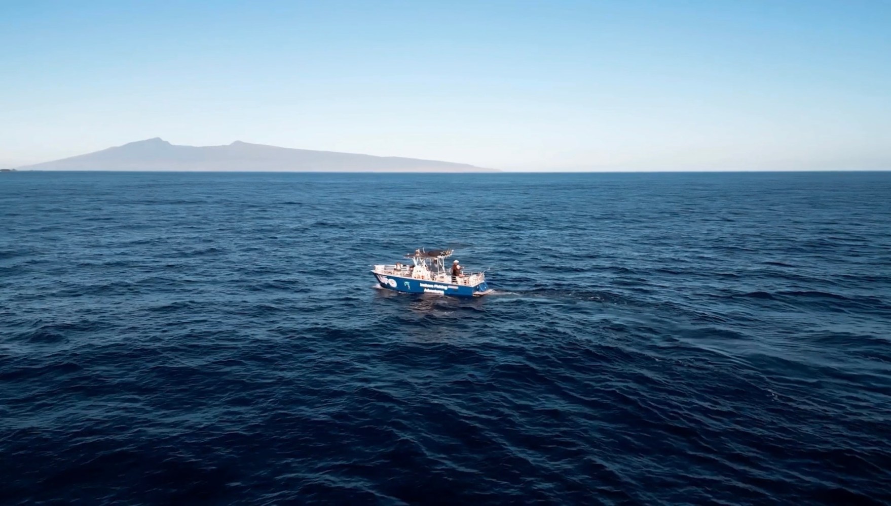 Small blue boat on open sea with mountains in the background.